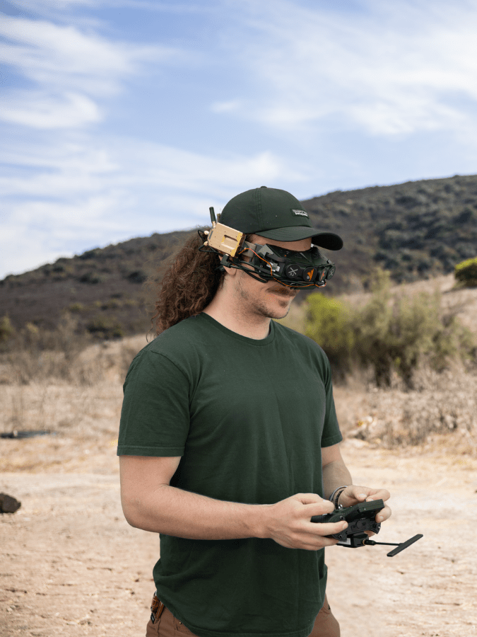 A ModalAI pilot wearing FPV goggles and holding a controller on a hillside.