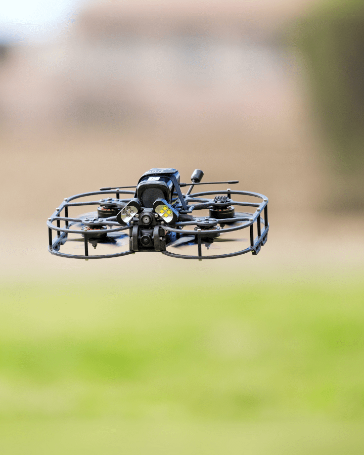A Stinger Vision FPV drone hovering low over a grass field.